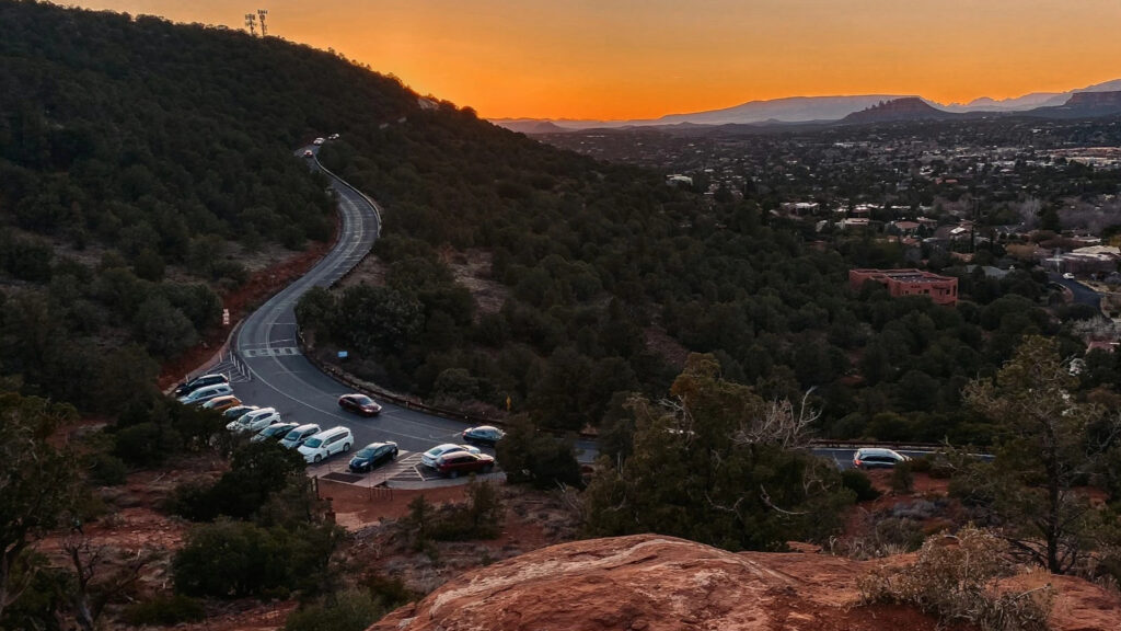 Busy parking lot at Fay Canyon Arch Hike trailhead in Sedona with red rock background.